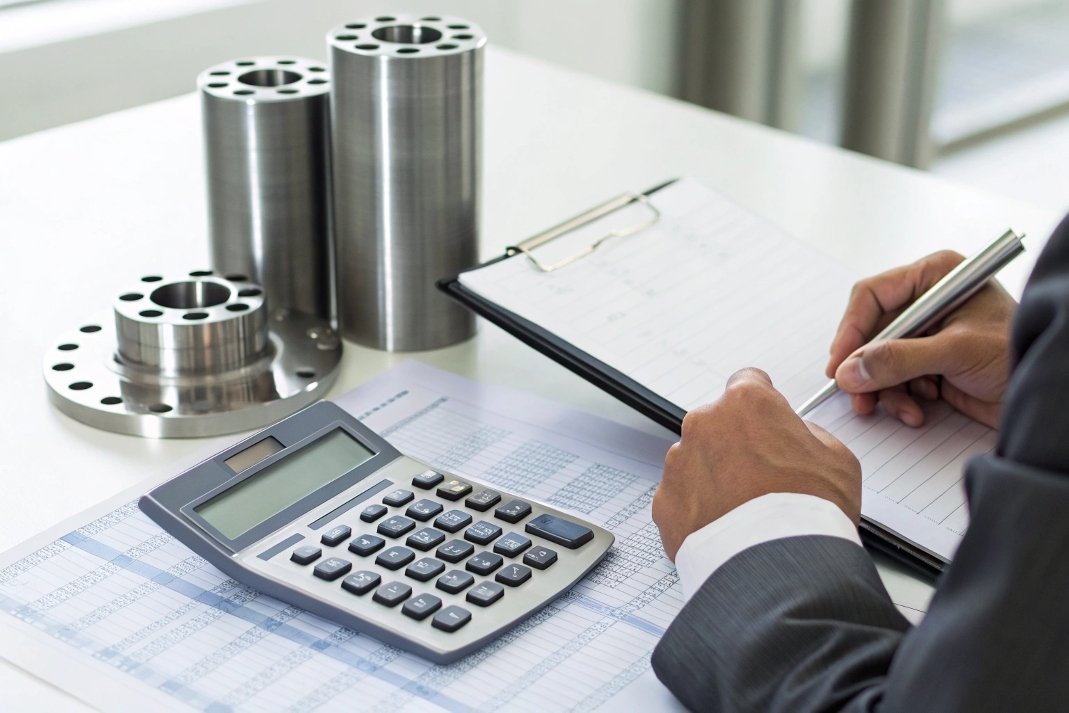 Person reviewing mechanical parts, using calculator and notepad, cost estimation, B2B supply chain