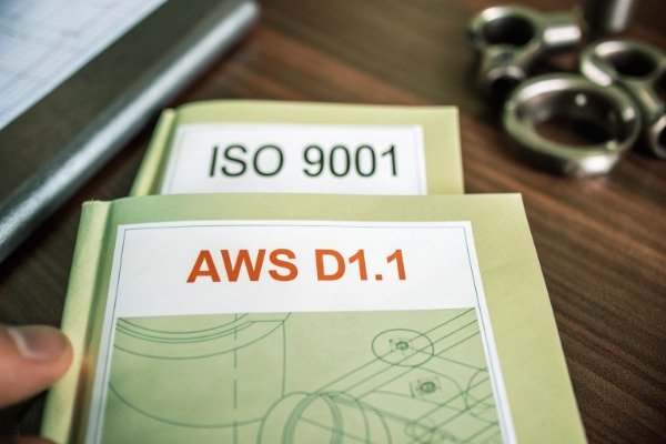 Stack of official ISO 9001 and AWS D1.1 welding certification documents on a desk (ID#1)
