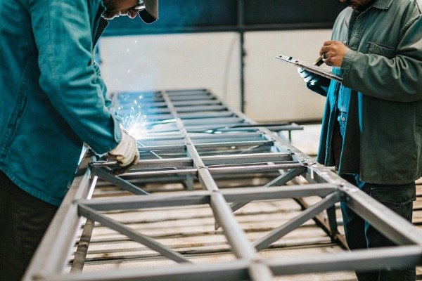 Workers welding metal frame in workshop (ID#2)