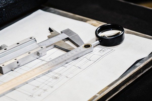 Meticulously measured metal stamping part with calipers and technical drawing on table (ID#4)