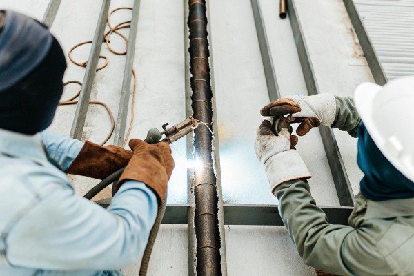 Two workers welding metal pipe indoors (ID#4)