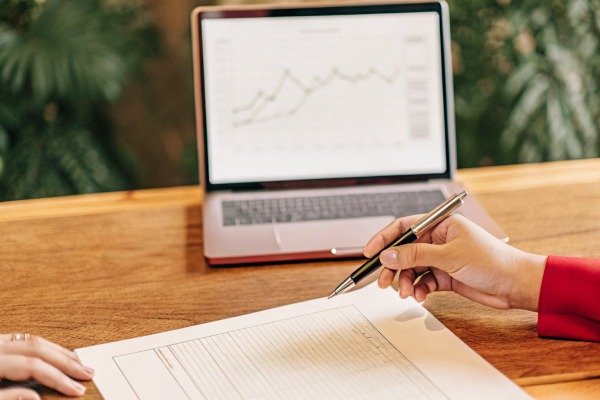 Person pointing at document with laptop in background (ID#2)