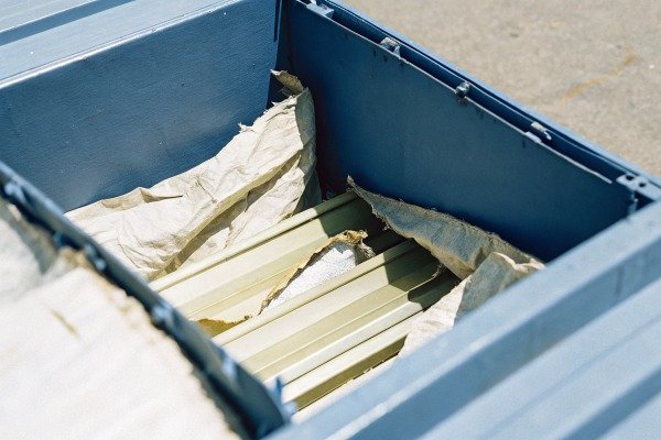 Metal parts wrapped in paper inside blue crate (ID#3)