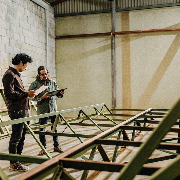 Two workers inspecting metal framework indoors (ID#1)