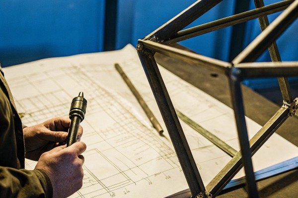 Worker holding tool near metal frame and blueprint (ID#5)