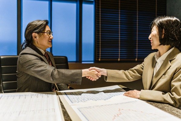 Two businesswomen shaking hands over charts (ID#3)