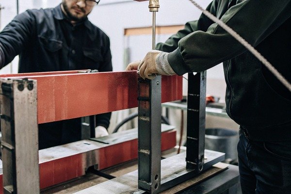 Workers handling red metal beam in workshop (ID#5)