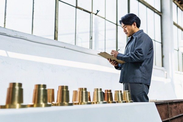 Worker inspecting brass parts with clipboard (ID#2)