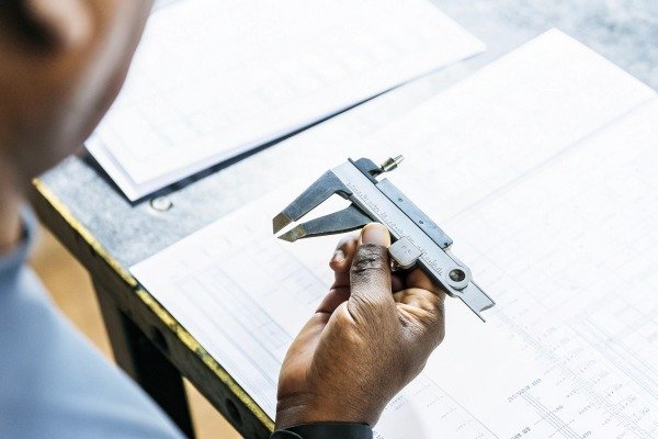 Close-up of hand measuring with caliper on blueprint (ID#2)