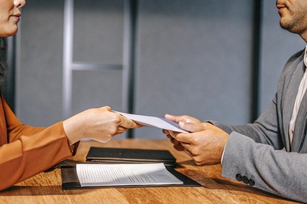 Two people exchanging documents at table (ID#4)