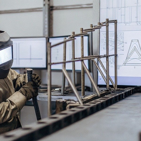 Сварщик работает над металлическим каркасом с чертежами (ID#1)