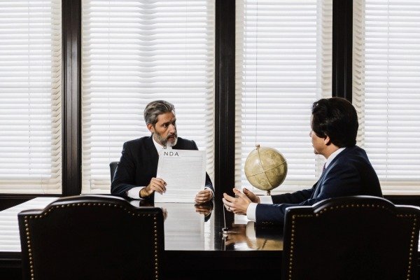 Two men discussing NDA document in office (ID#4)