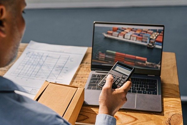 Man calculating shipping costs with laptop and package (ID#2)