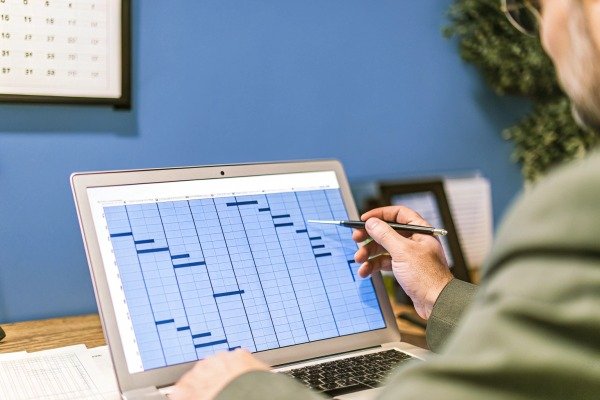 Person pointing at project schedule on laptop (ID#5)